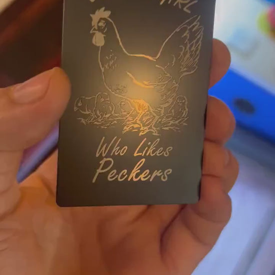 Human hand showcasing engraved humorous gift card in black and silver metal with chicken artwork for Friendsgiving