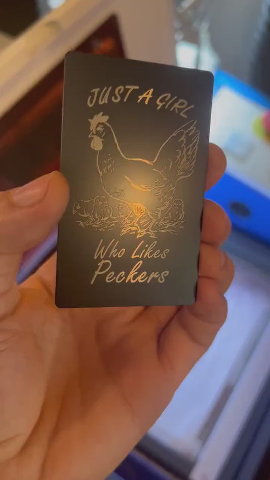 Human hand showcasing engraved humorous gift card in black and silver metal with chicken artwork for Friendsgiving