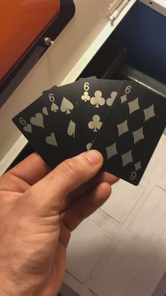 Close up video of hand holding 4 laser engraved metal playing cards with 6 of hearts, 6 of spades, six of clubs and six of diamonds cards