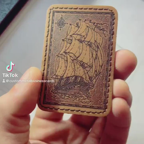 hand holding laser engraved brown leather patch, rotating to demonstrate sailship design
