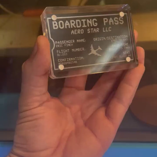 Hand holding a laser engraved black/silver  metal boarding pass graphic with personalized text, shown in optional acrylic display case