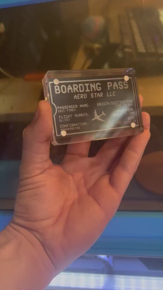 Hand holding a laser engraved black/silver  metal boarding pass graphic with personalized text, shown in optional acrylic display case
