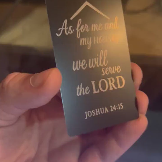 Hand holding a laser engraved metal keepsake card with "As For Me And My House, We Will Serve The Lord" typography text and Joshua 24:15 bible verse reference