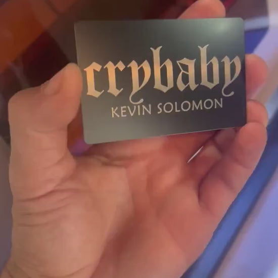 Hand holding laser engraved metal cry baby club keepsake card with personalized name engraving text in black/silver