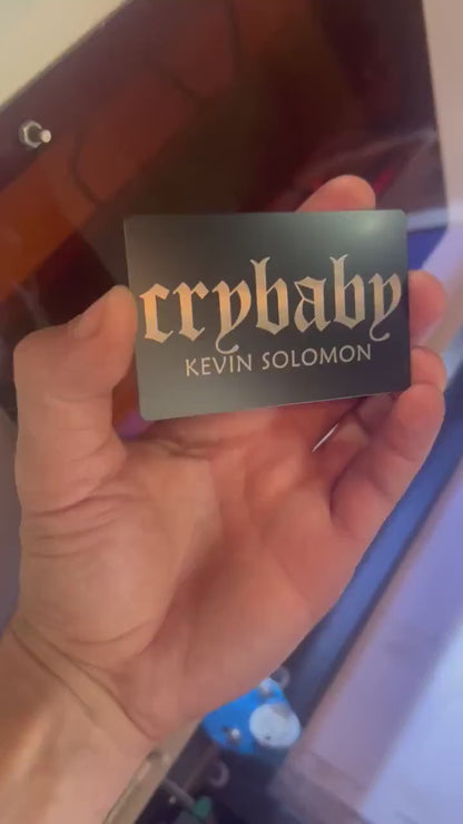Hand holding laser engraved metal cry baby club keepsake card with personalized name engraving text in black/silver