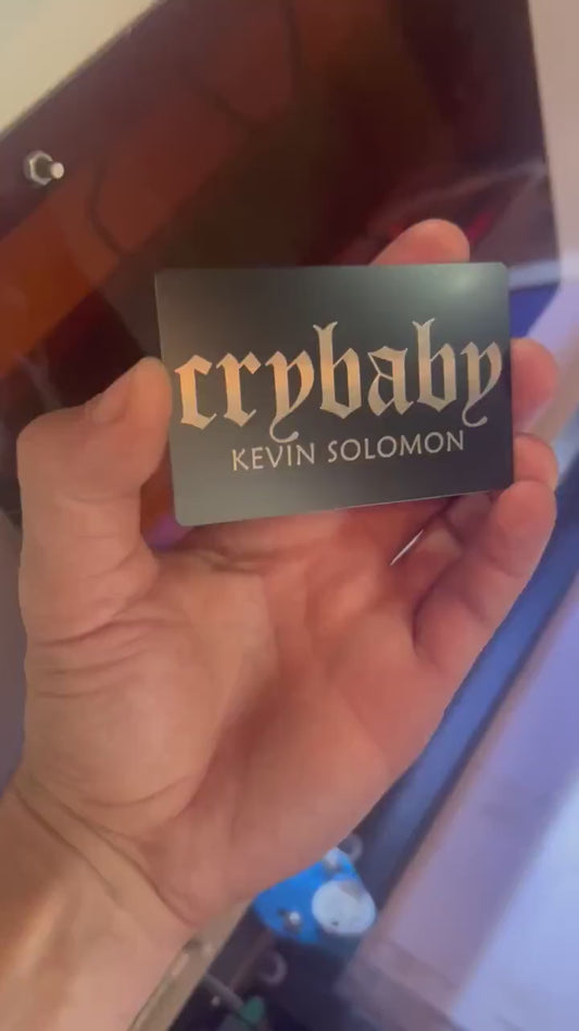 Hand holding laser engraved metal cry baby club keepsake card with personalized name engraving text in black/silver