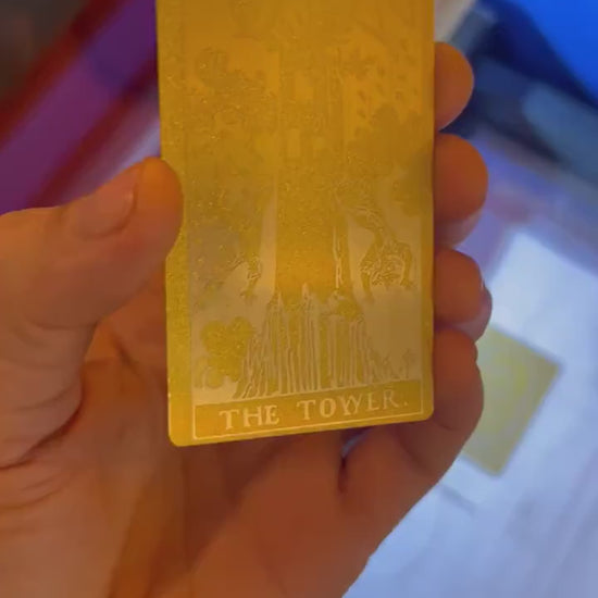 Close up video of hand holding a laser engraved metal tarot card in Gold/Silver with The Tower artwork