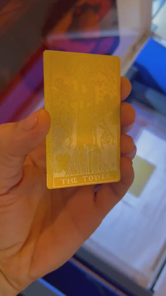 Close up video of hand holding a laser engraved metal tarot card in Gold/Silver with The Tower artwork
