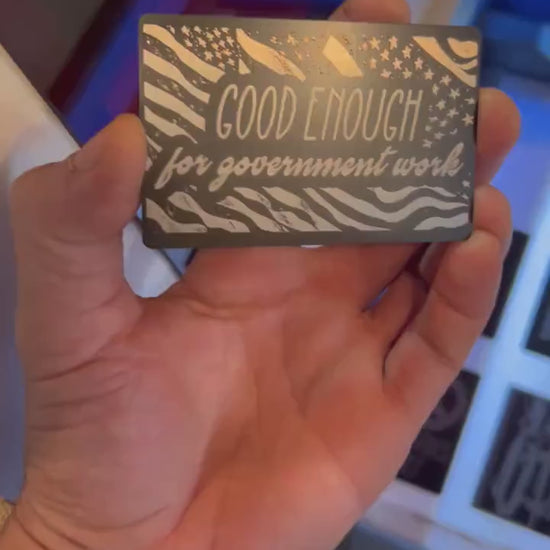 Hand holding a laser engraved metal keepsake card with "Good Enough For Government Work" funny phrase engraving, in Black/Silver anodized aluminum