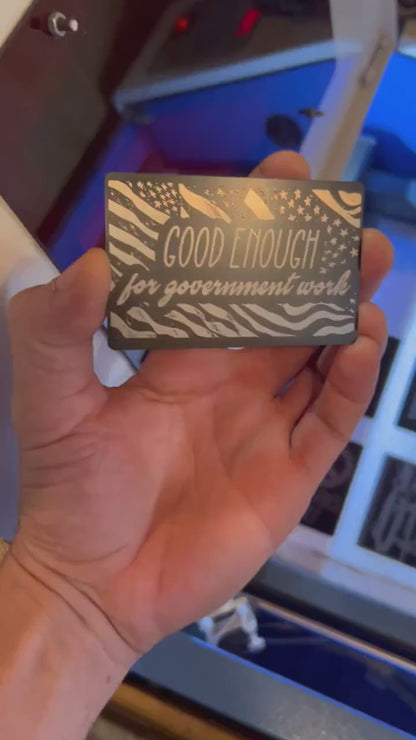 Hand holding a laser engraved metal keepsake card with "Good Enough For Government Work" funny phrase engraving, in Black/Silver anodized aluminum