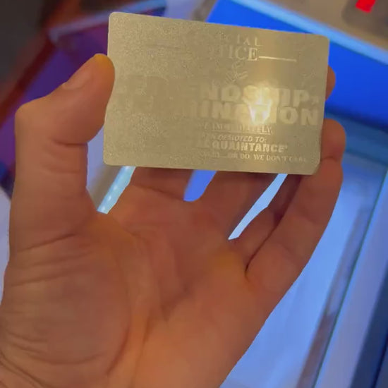 Close up video of hand holding a laser engraved metal gift card with Friendship Termination funny gag gift card text, in Silver/Silver