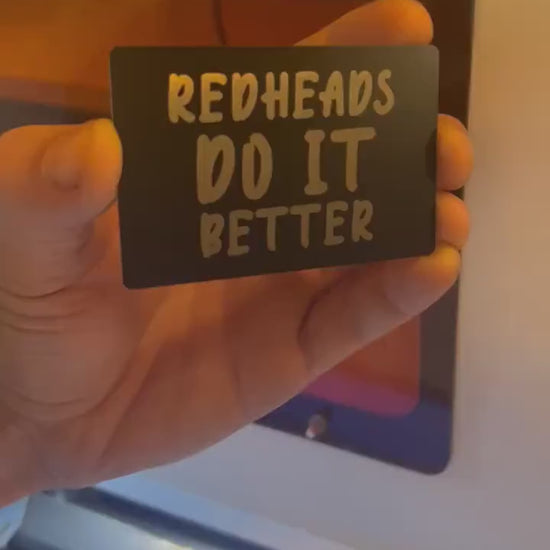 Close up video of hand holding a laser engraved funny metal gift card with Red Heads Do It Better sarcastic text