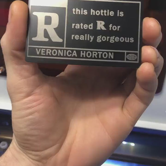 Close up video of hand holding a laser engraved metal This Hottie Is Really Gorgeous, Rated R with custom name engraving below keepsake gift card