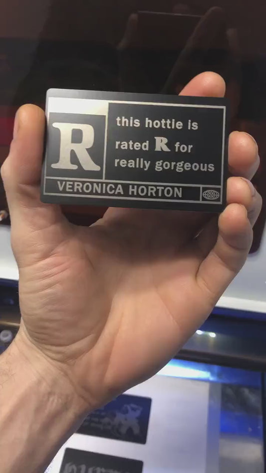 Close up video of hand holding a laser engraved metal This Hottie Is Really Gorgeous, Rated R with custom name engraving below keepsake gift card