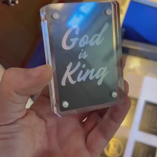 Hand holding a laser engraved black/silver God is King metal bookmark card, shown in optional acrylic display case