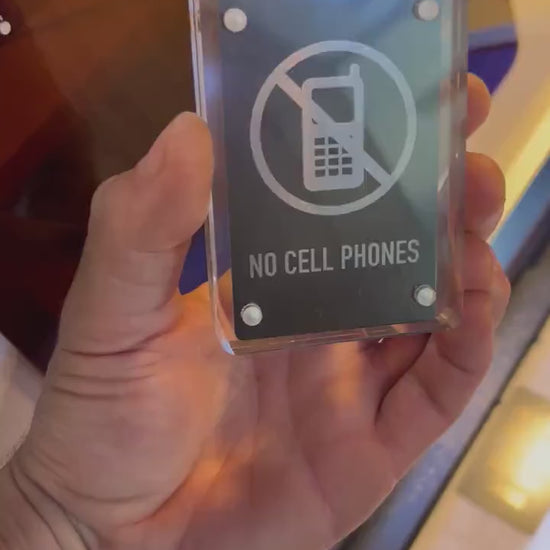 Hand holding a laser engraved black/silver No Cell Phones metal signage shown in optional acrylic display case