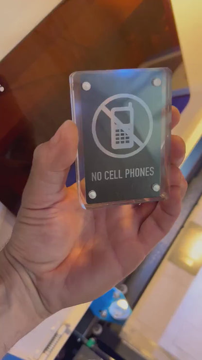 Hand holding a laser engraved black/silver No Cell Phones metal signage shown in optional acrylic display case