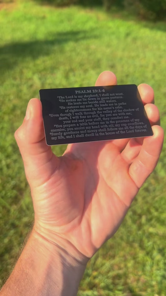 Hand holding a laser engraved metal bible verse card in front of a natural background