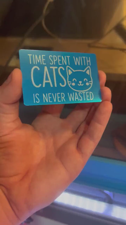 Hand holding a laser engraved metal pet lover gift that reads "Time Spent With Cats Is Never Wasted", with cute kitten graphic in blue/silver anodized aluminum