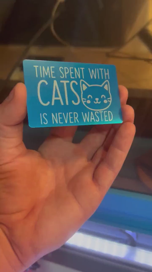 Hand holding a laser engraved metal pet lover gift that reads "Time Spent With Cats Is Never Wasted", with cute kitten graphic in blue/silver anodized aluminum