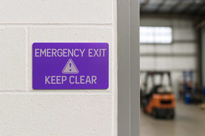 Purple emergency exit sign on a white wall with a blurred warehouse background