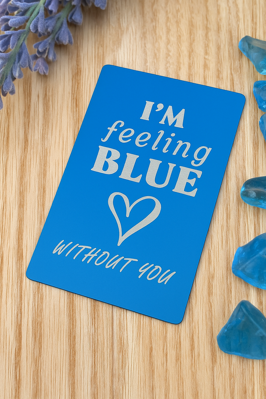 Blue/silver metal engraved romantic gift card with 'I'm feeling BLUE without you' text on a wooden surface with blue decorative elements.