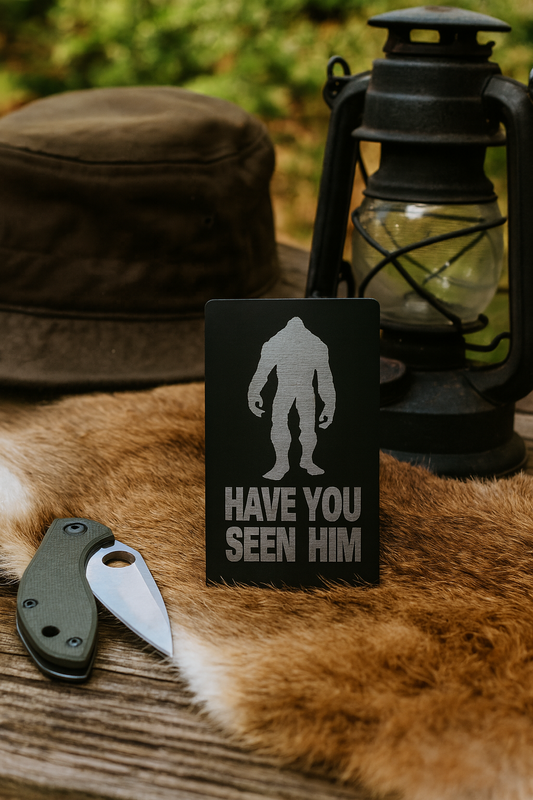 Black metal keepsake plaque with Bigfoot silhouette and 'Have You Seen Him?' text on a wooden surface with a hat and lantern in the background.