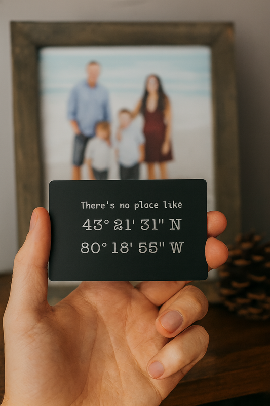 Hand holding a metal laser engraved keepsake card with custom quote and GPS coordinates in front of a framed family photo.