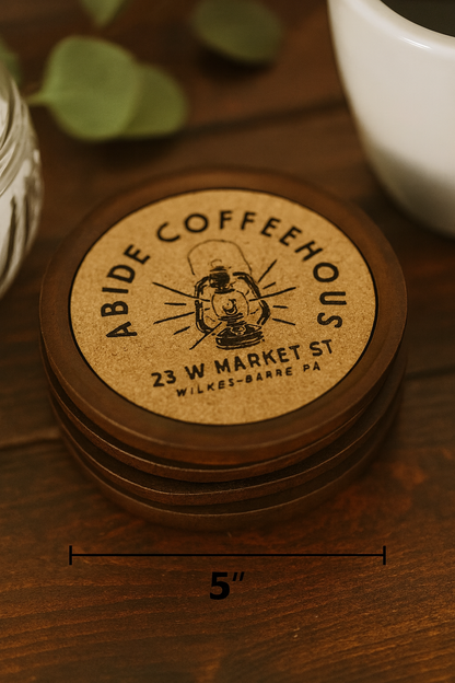 Stack of cork/wood Coffeehouse coasters on a wooden surface with a cup in the background.