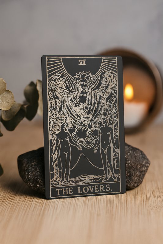 Metal Tarot card titled 'The Lovers' on a wooden surface with a blurred background