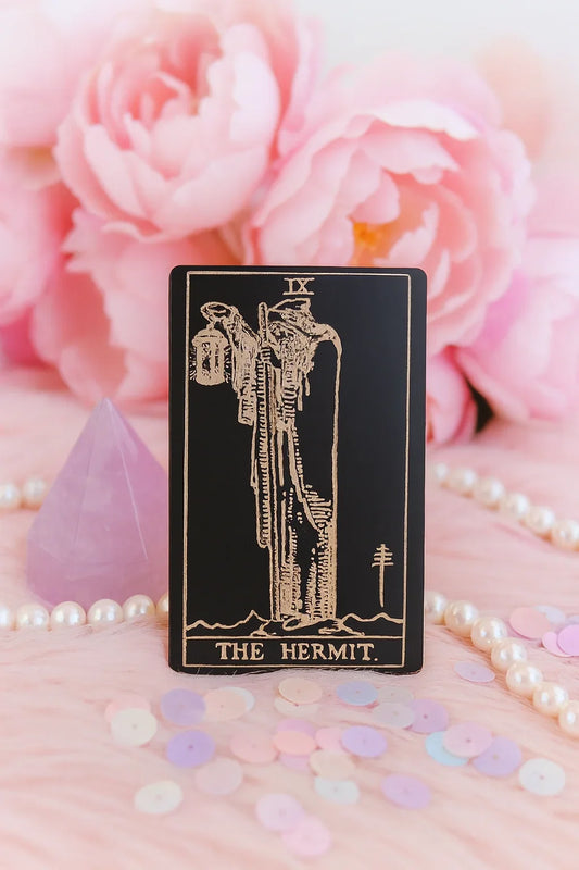 Metal Tarot card titled 'The Hermit' with pink flowers and pearls in the background