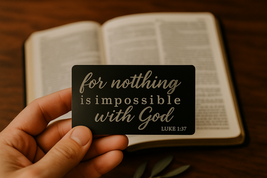 Hand holding a card with 'For nothing is impossible with God' text in front of an open book.