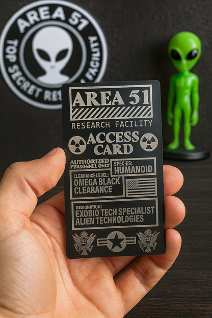 Hand holding metal laser engraved Area 51 research facility access card novelty gift with a green alien figure and logo in the background.