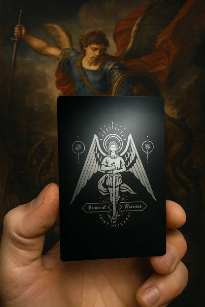 Hand holding a black card with an St Michael angelic design against a dark background