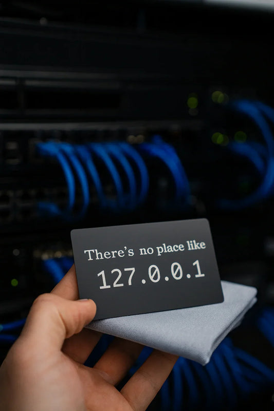 Hand holding a card with 'There's no place like 127.0.0.1' text in front of network cables.