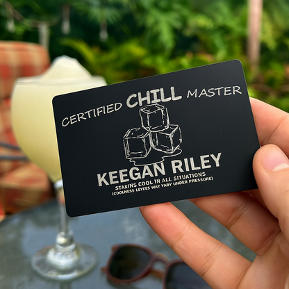 Black card with 'Certified Chill Master' text and ice cube illustration, held in front of a blurred outdoor setting with a drink and sunglasses.