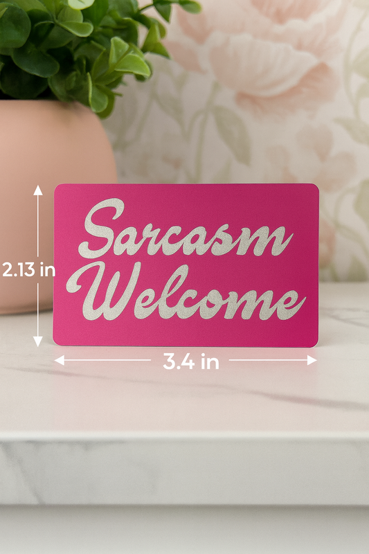 Pink sign with 'Sarcasm Welcome' text and measurements on a white surface with decorative elements.