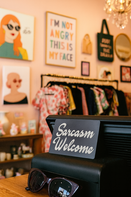 Store interior with metal 'Sarcasm Welcome' sign leaning on cash register