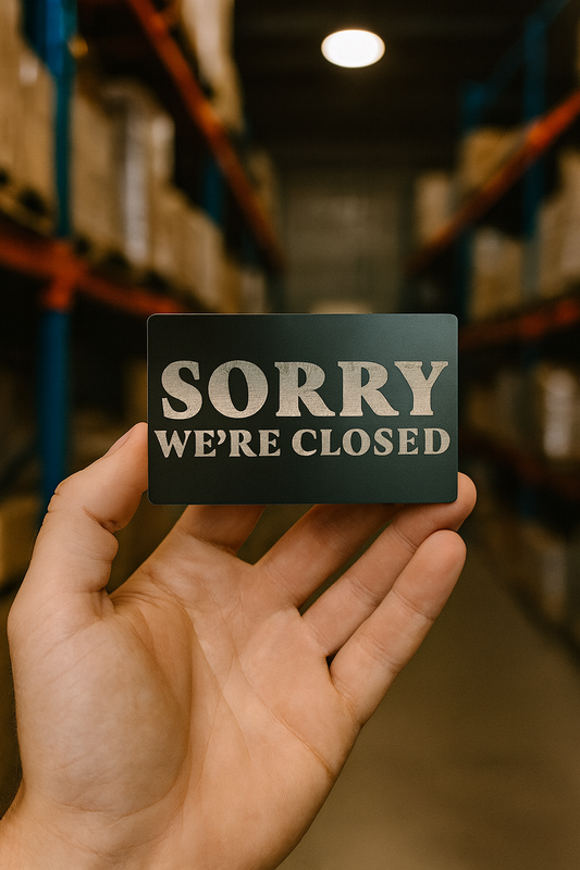 Hand holding a 'Sorry, We're Closed' sign in a warehouse setting