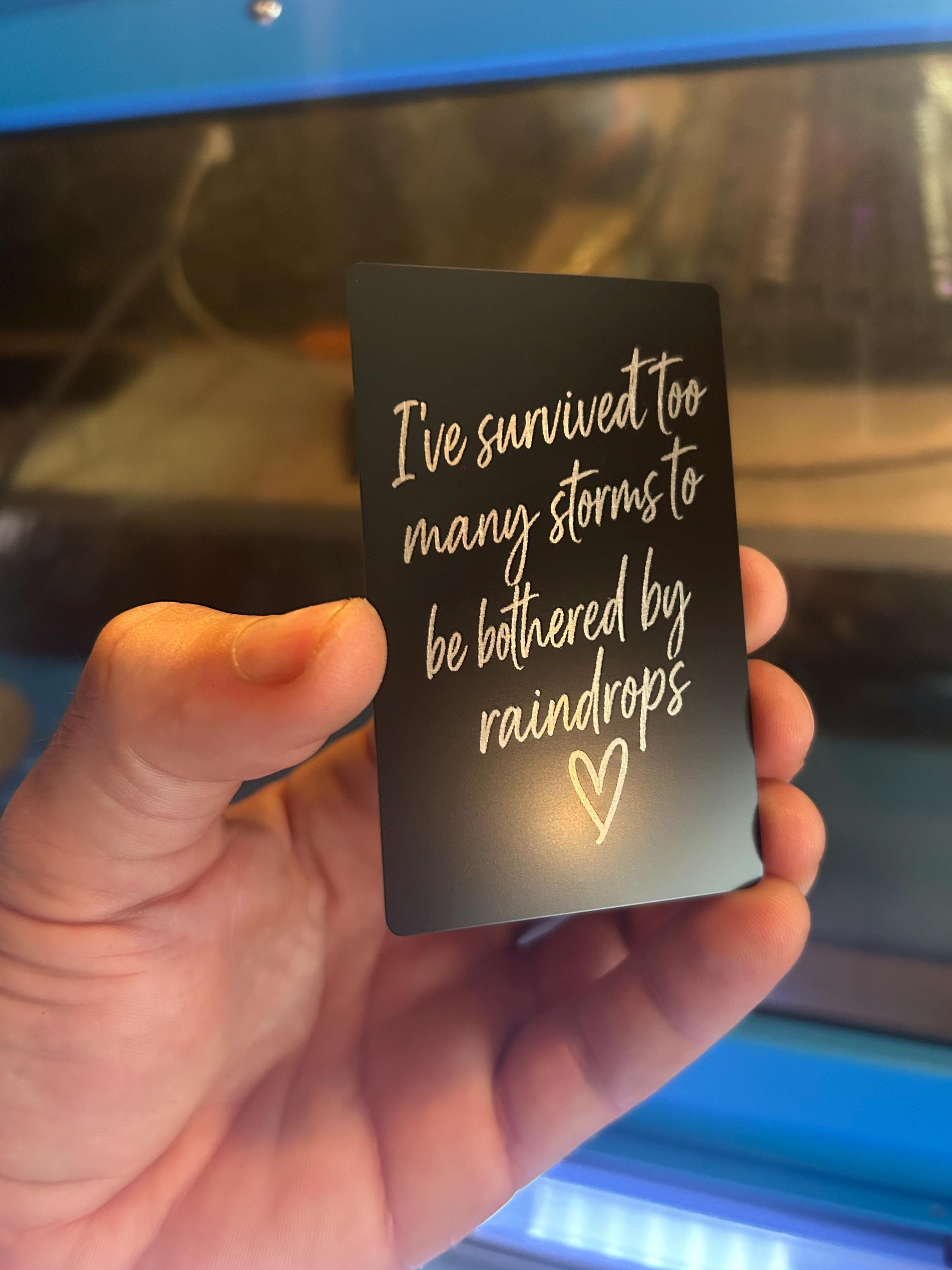 Close-up of engraved anodized aluminum inspirational card featuring rainstorm quote with hand drawn heart design