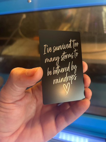 Close-up of engraved anodized aluminum inspirational card featuring rainstorm quote with hand drawn heart design