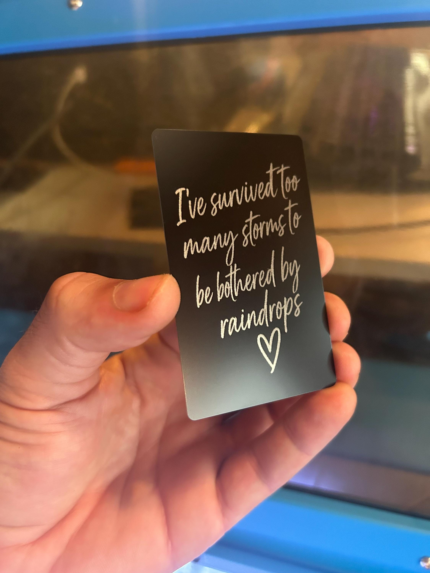 Angled view of custom black/silver engraved metal keepsake card engraved with motivational phrase and heart artwork