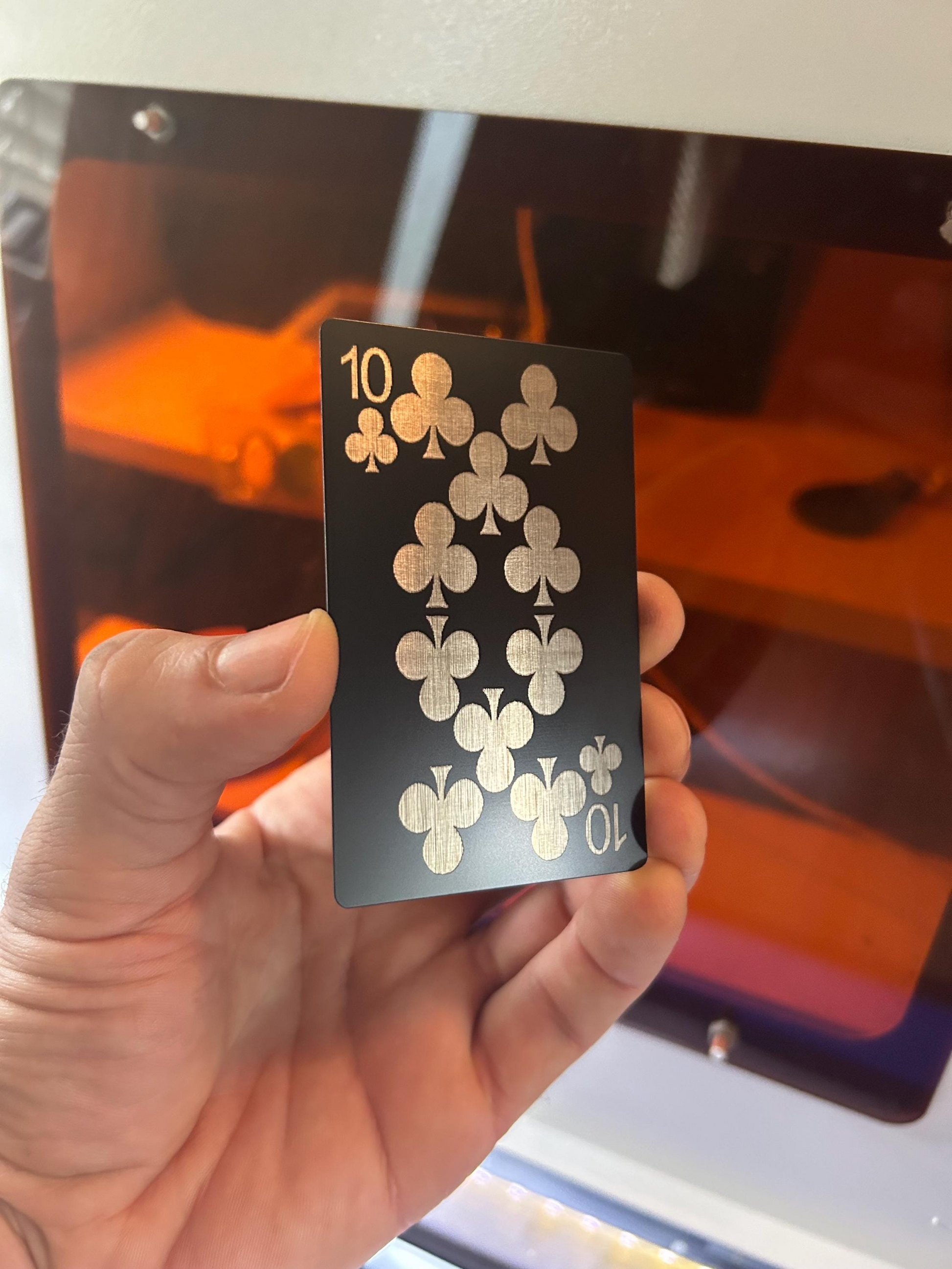 Hand holding a ten of clubs laser engraved poker card in front of a machine
