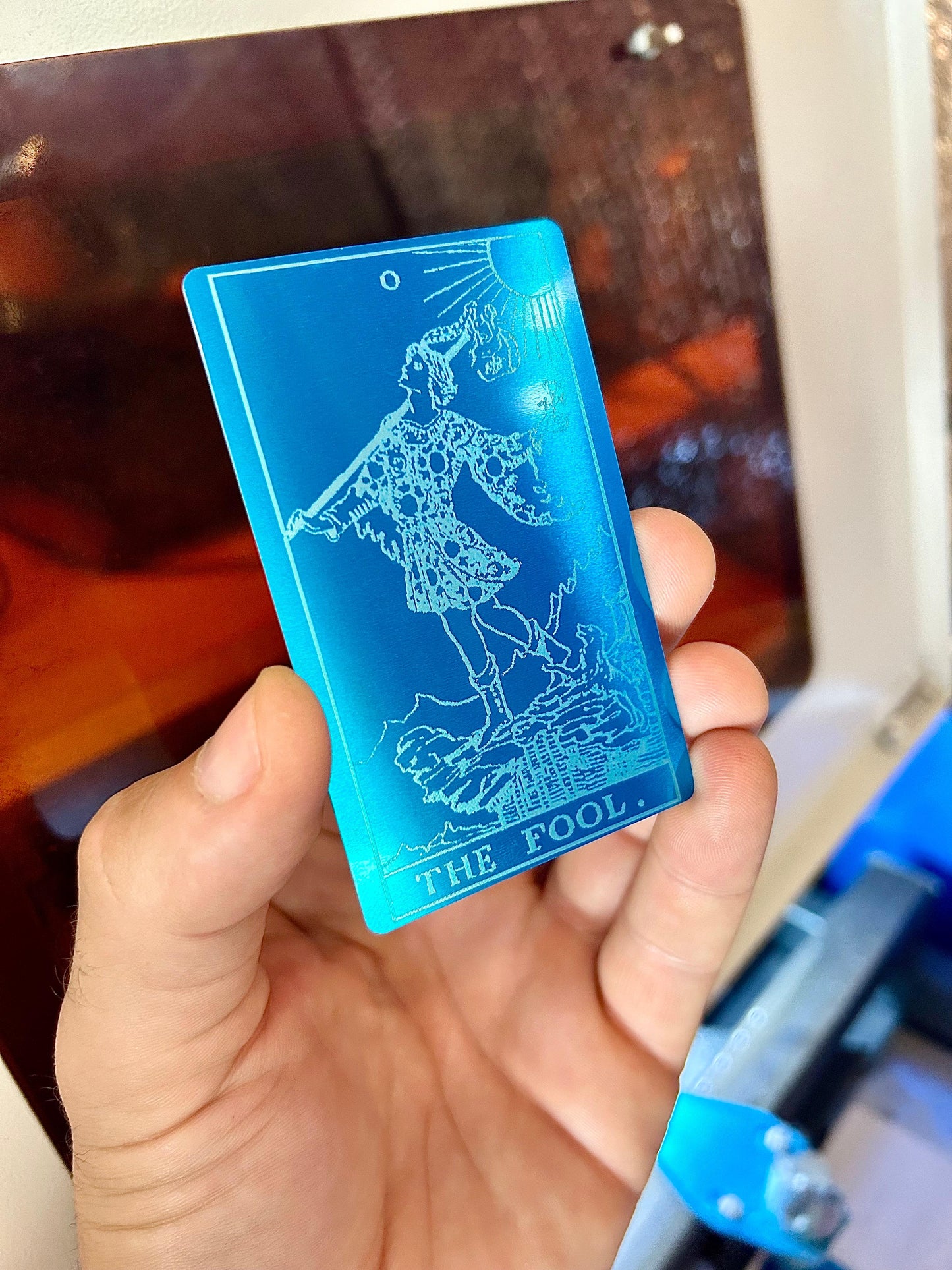 Metal tarot card with "The Fool" laser engraving in blue/silver anodized aluminum