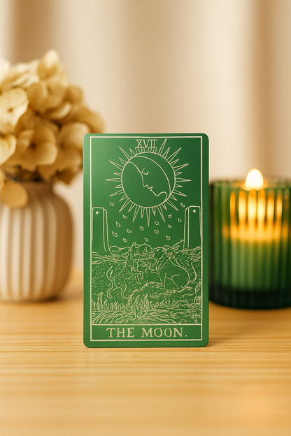 Green/silver metal tarot card engraving  titled 'The Moon' on a wooden surface with decorative elements.
