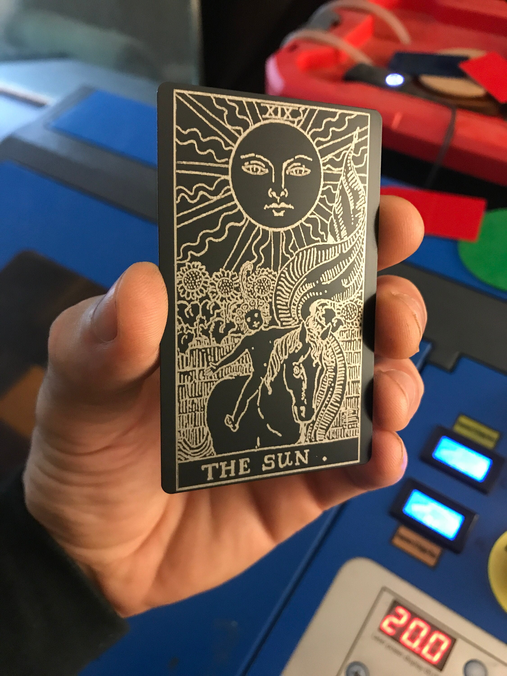 laser engraved metal keepsake in hand, with the sun tarot card design in matte black/silver