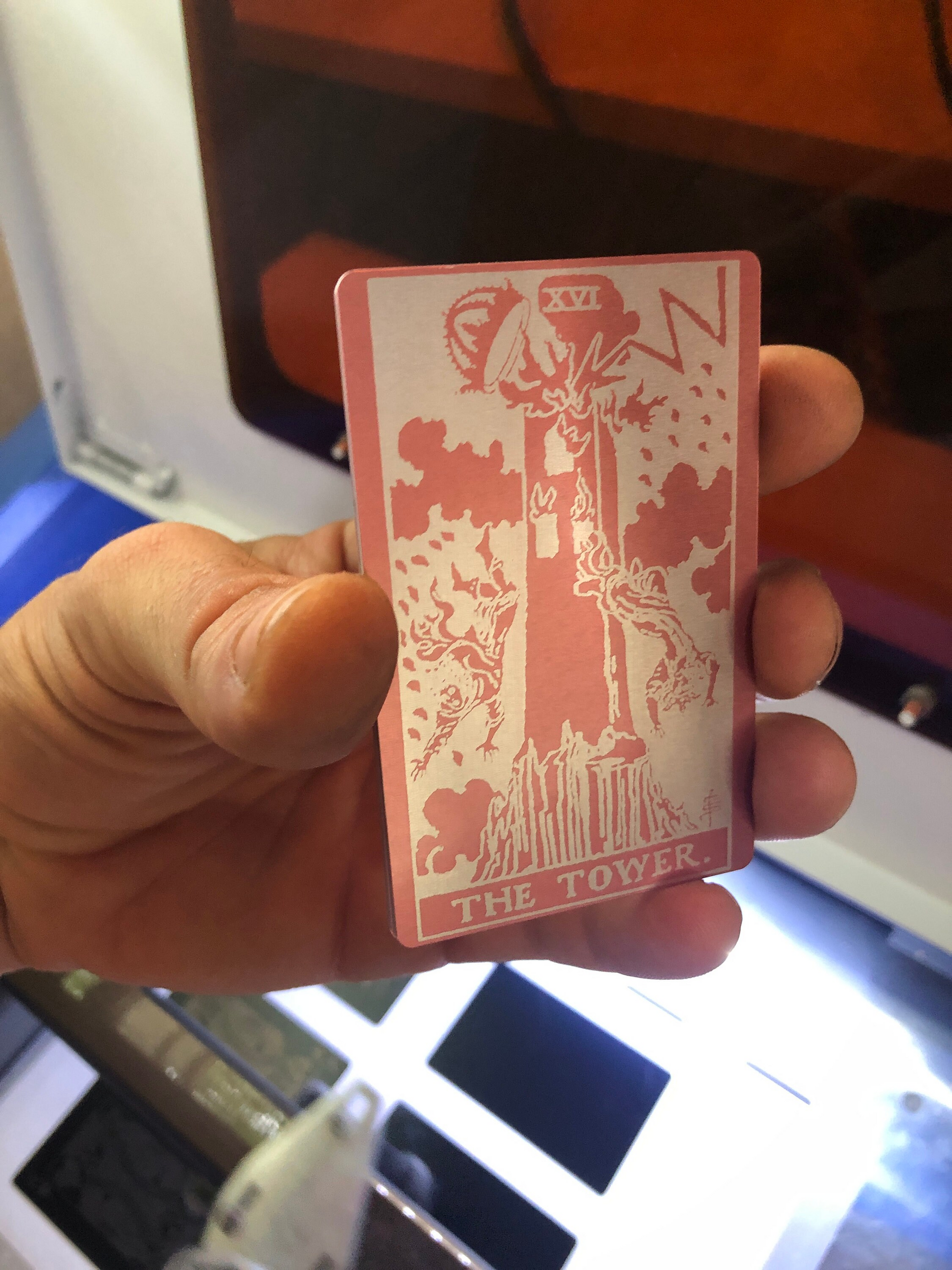 Rose gold/silver metal tarot card with 'The Tower' tarot card design held by a hand.