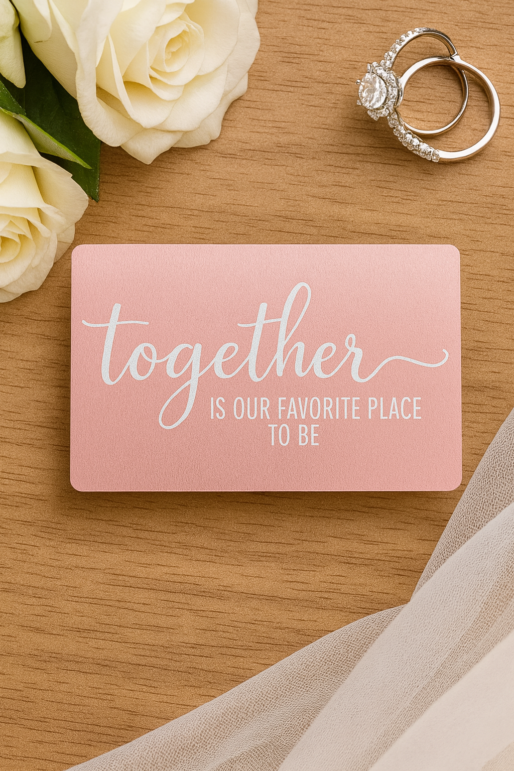 Pink card with 'Together is our favorite place to be' text, ring, and white roses on a wooden surface