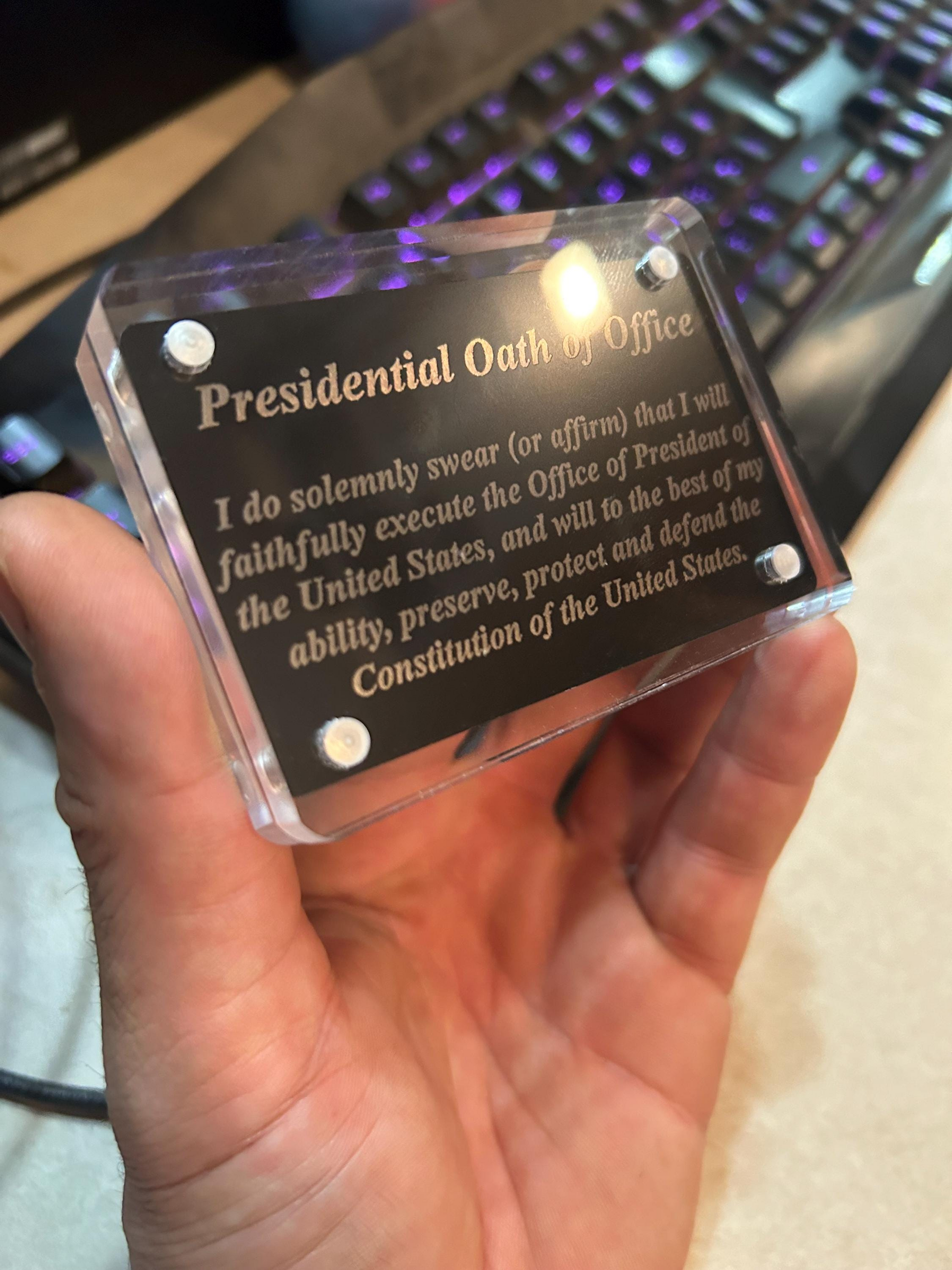 Hand holding a transparent acrylic display case with magnetic closure, with example laser engraved metal business card inside with text