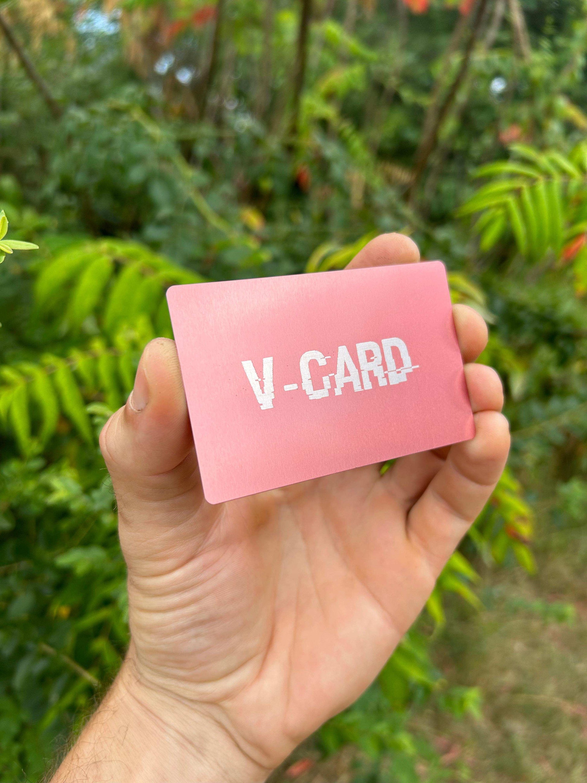 Hand holding a rose gold metal card with 'V-CARD' text against a green leafy background
